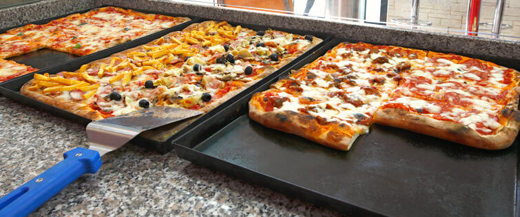 Counter of the pizzeria with trays and square pieces of pizz