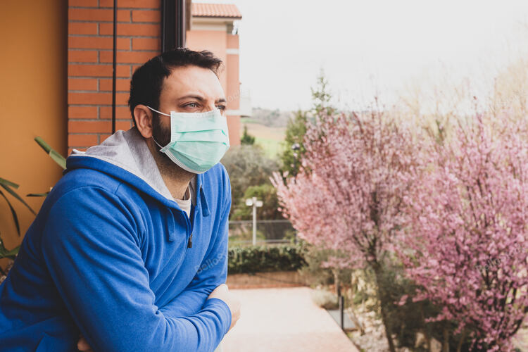 Young caucasian man with mask looking out on the terrace of 