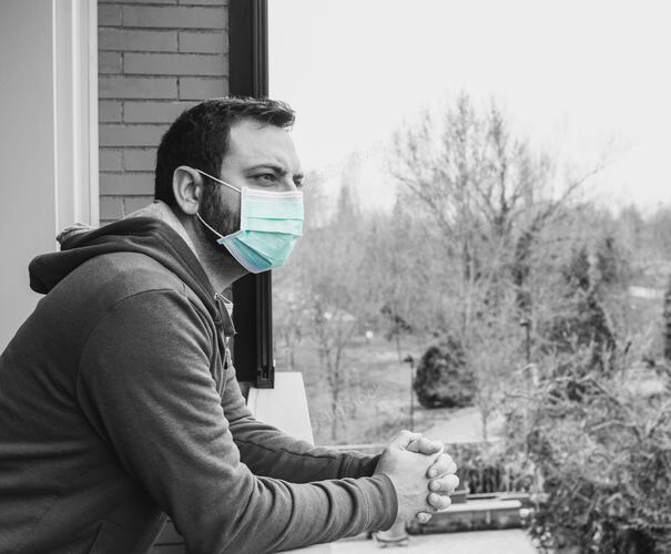 Young caucasian man with mask looking out onto home terrace 