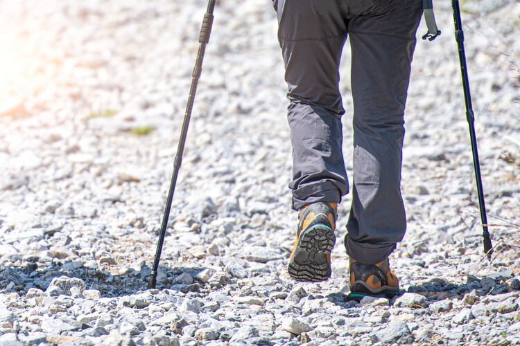 Detail of mountain walker on stony road with Nordic walking 