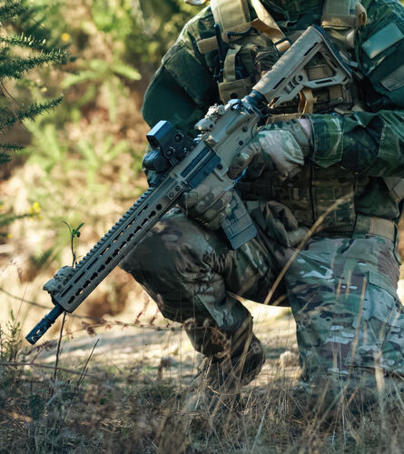 Kneeling in a dense forest, an airsoft player dons a camoufl
