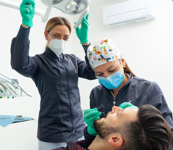 Female dentist examines a man patient in a dental office usi