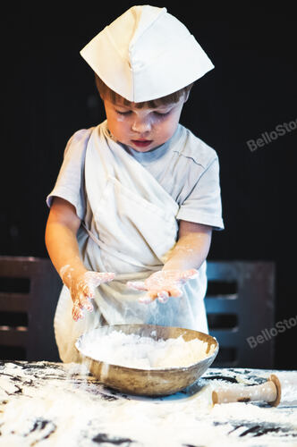 A child kneads flour on a dark background