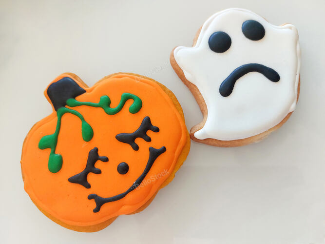 Two halloween cookies depicting a pumpkin and a sad ghost, iced and decorated with black and green f