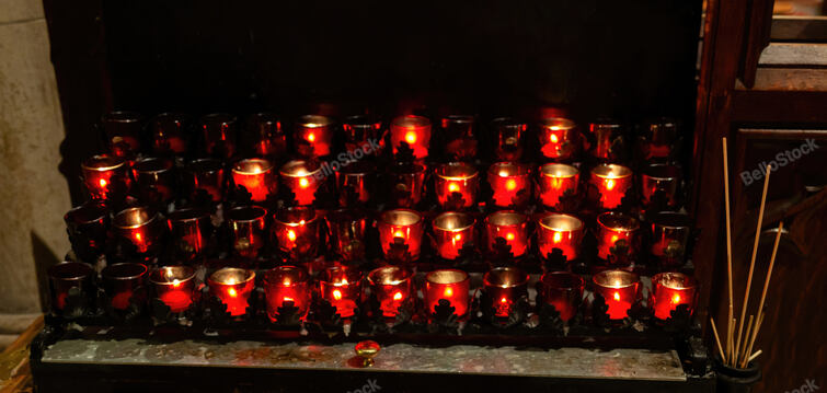 Rows of red votive candles glowing in a dim church interior, evoking prayer, rem