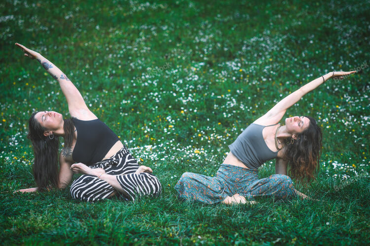 Couple of friends practice meditative yoga in a spring flowe