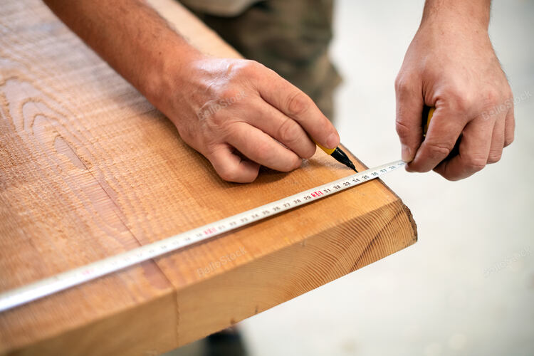 Carpenter measuring a wooden plank with a tape measure and m