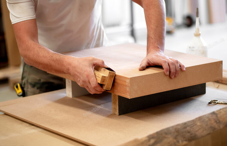Hands of a carpenter manually sanding the edge of a wooden b